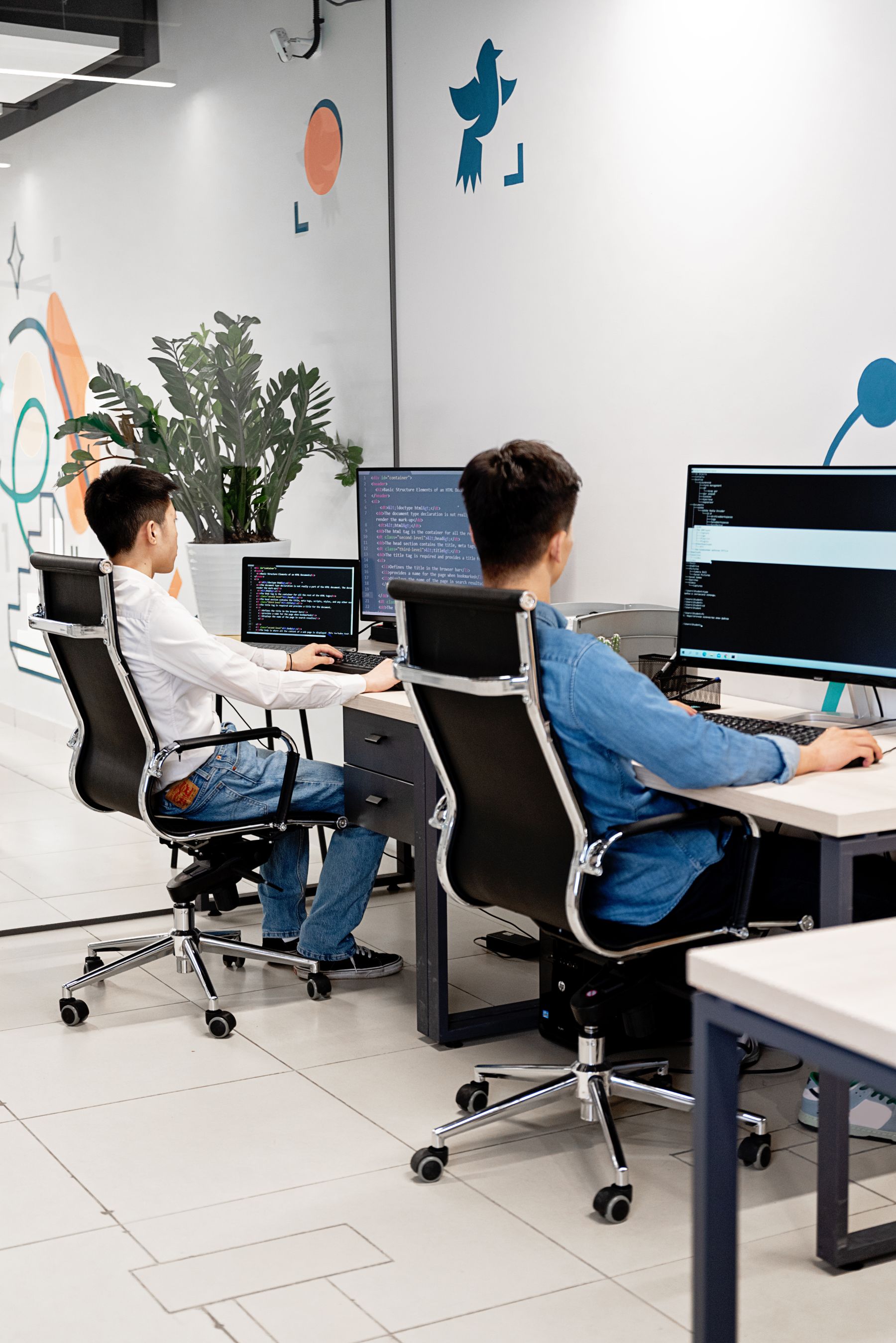 Two developers writing code at their desks in a bright office